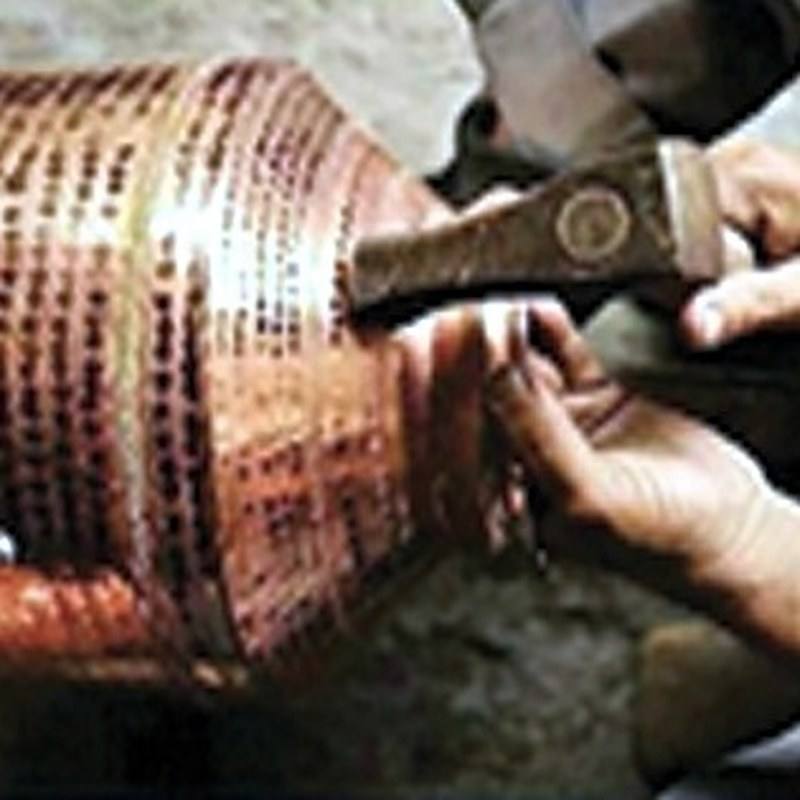 A craftsman hand hammering a large copper vessel